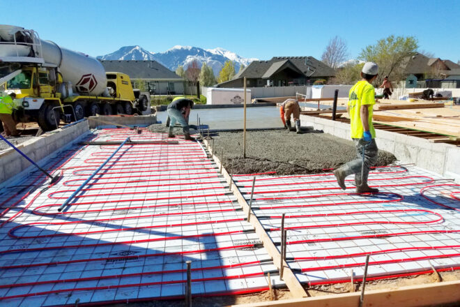 Workers pour concrete foundation with radiant floor heating for a custom home by Precision Homes & Design.