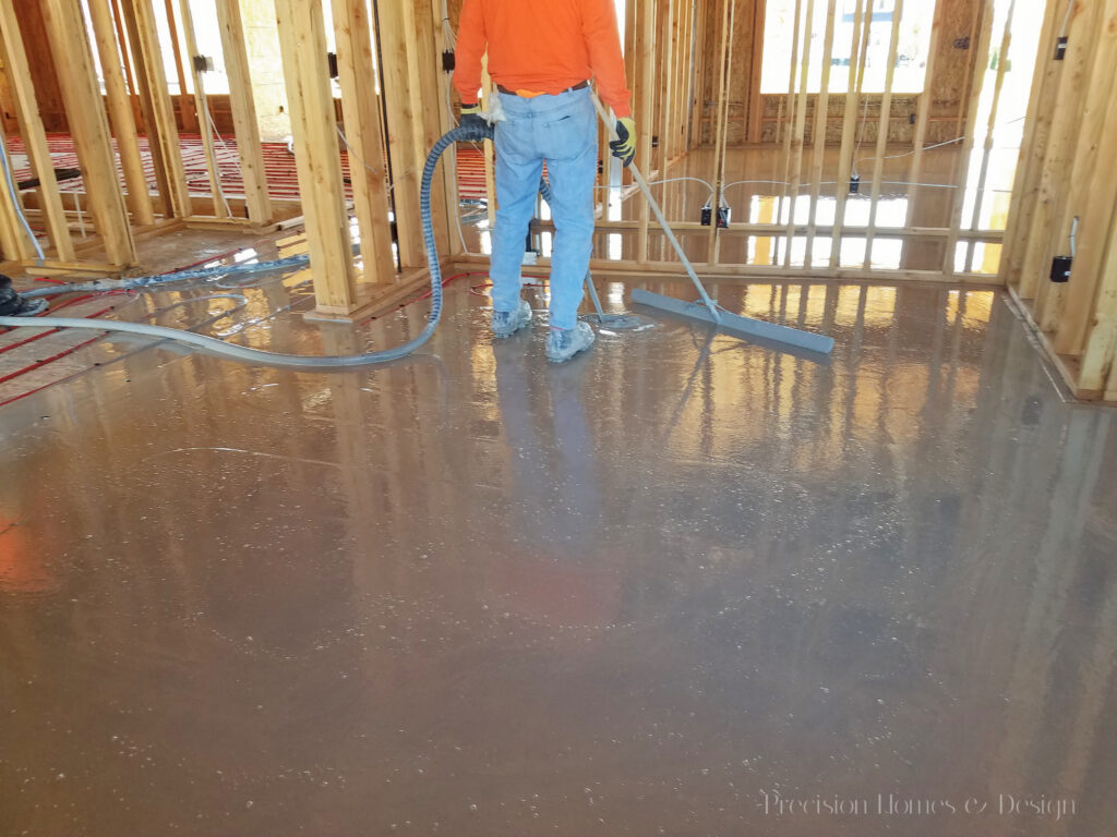 Worker pouring and leveling wet concrete inside a new residential construction site.
