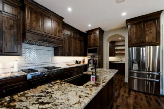 Luxury custom home kitchen with dark wood cabinets, granite island, stainless appliances, and elegant lighting.