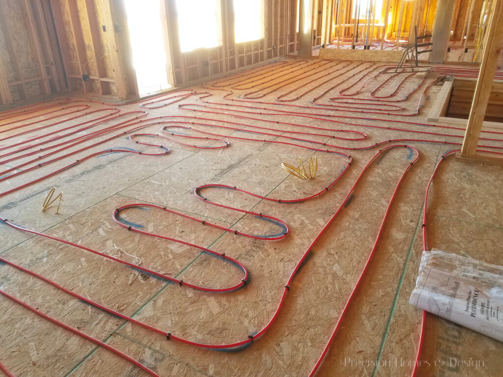 Unfinished interior with red radiant floor heating pipes, wooden studs, and bright natural light.